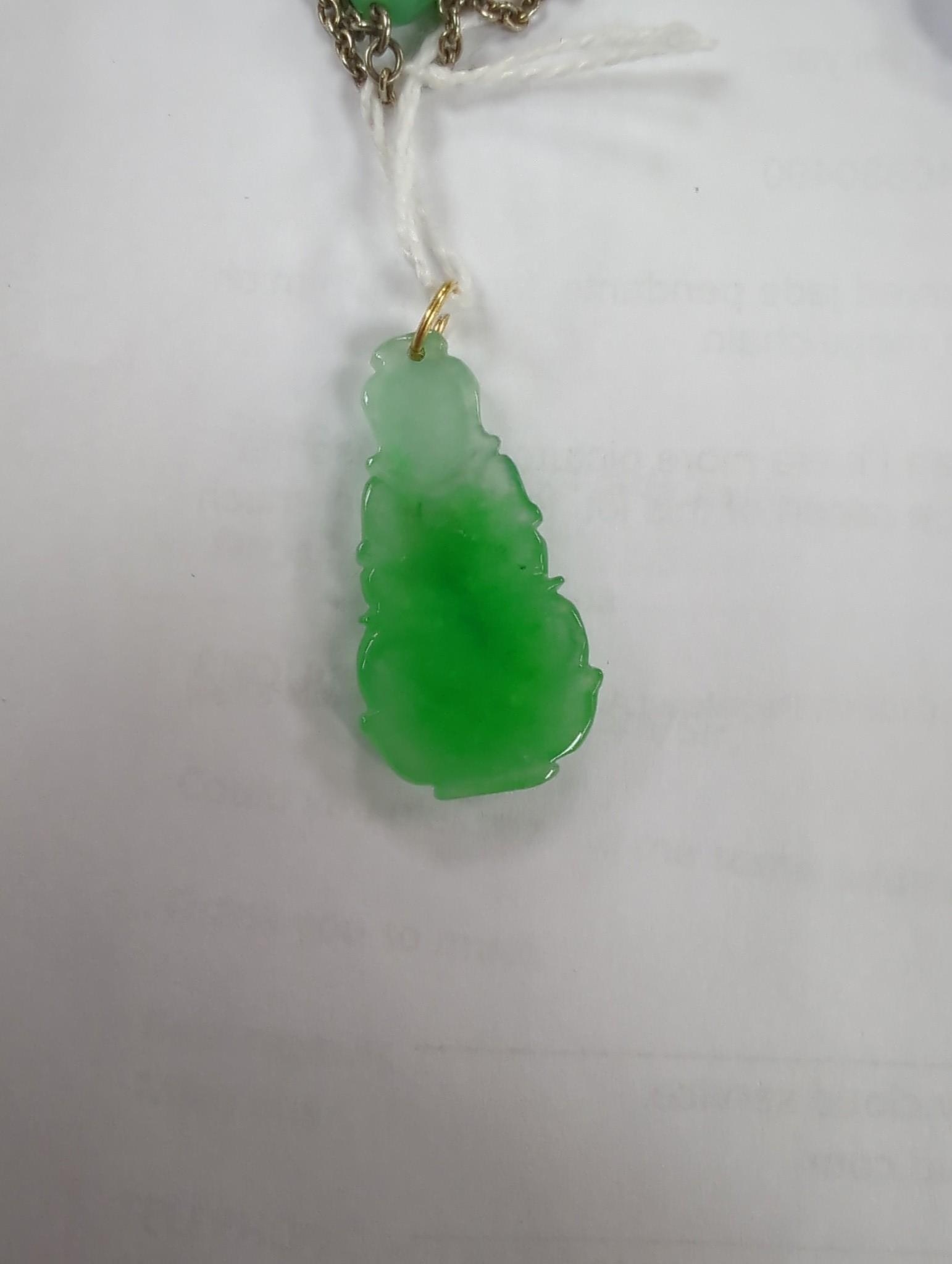 Two carved jade pendants, largest 47mm on a white metal chain.